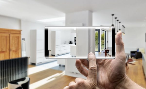 Two hands holding a Smartphone taking a picture in a newly remodeled luxury living room and kitchen